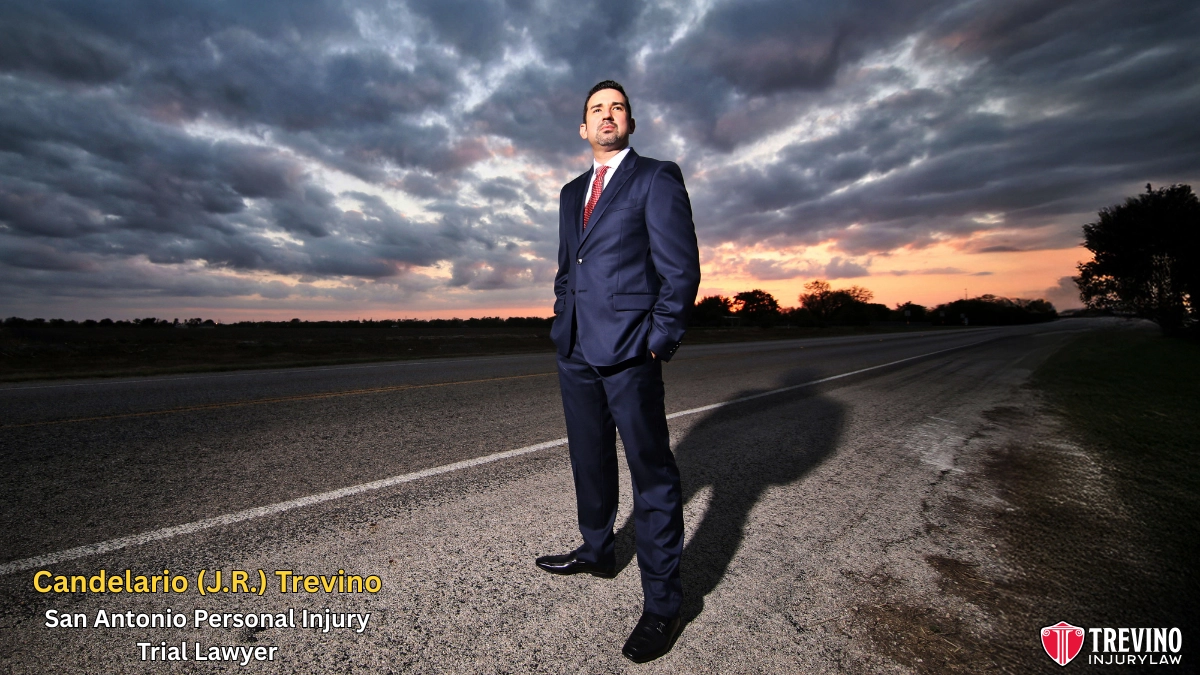 San Antonio personal injury trial lawyer, Candelario (J.R.) Trevino. wears a dark blue suit stands confidently on an empty rural road at sunset, with dramatic clouds in the sky. The text reads, "Candelario (J.R.) Trevino, San Antonio Personal Injury Trial Lawyer." The Trevino Injury Law logo appears in the lower right corner.