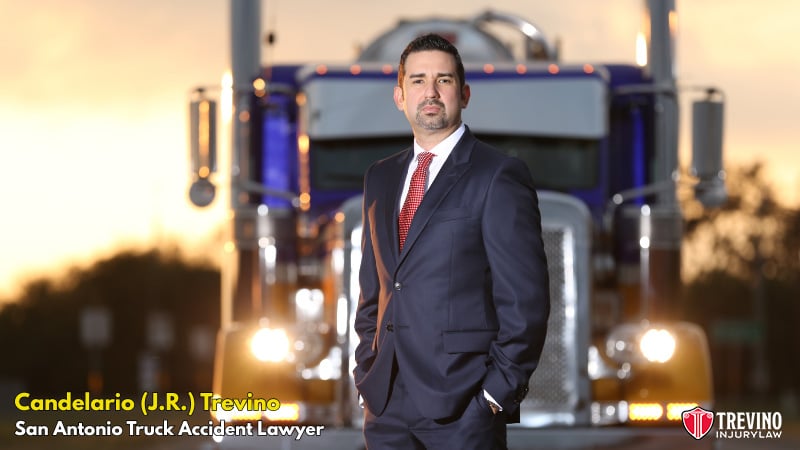 San Antonio truck accident lawyer near me. Truck accident lawyer Candelario (J.R.) Trevino, stands confidently in front of a large blue semi-truck at sunset. Text reads: u0022Candelario (J.R.) Trevino, San Antonio Truck Accident Lawyeru0022 with the Trevino Injury Law logo in the bottom right corner.